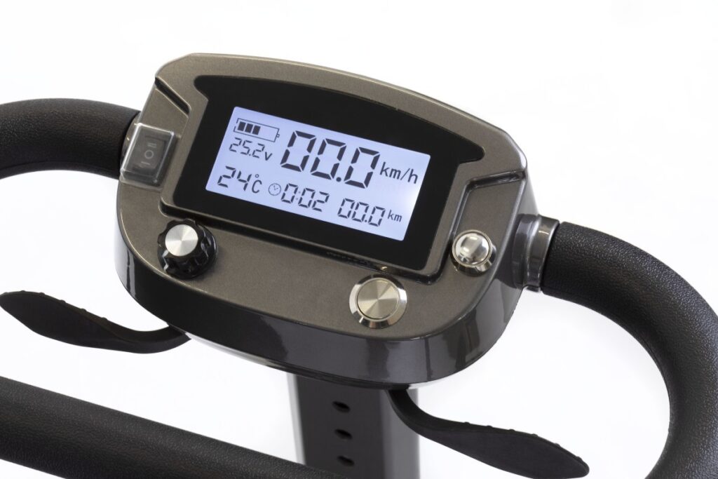 A close-up of a mobility scooter's control panel with a hand operating it, displaying battery level and speed settings.